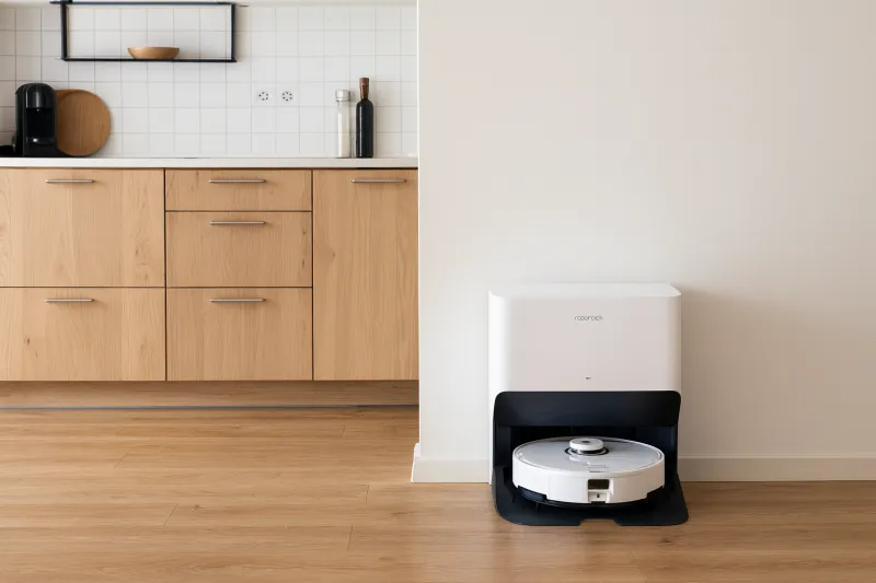 Roborock robotstøvsuger i dock placeret op ad en væg i et lyst dansk køkken med trægulv og lyse træskabe